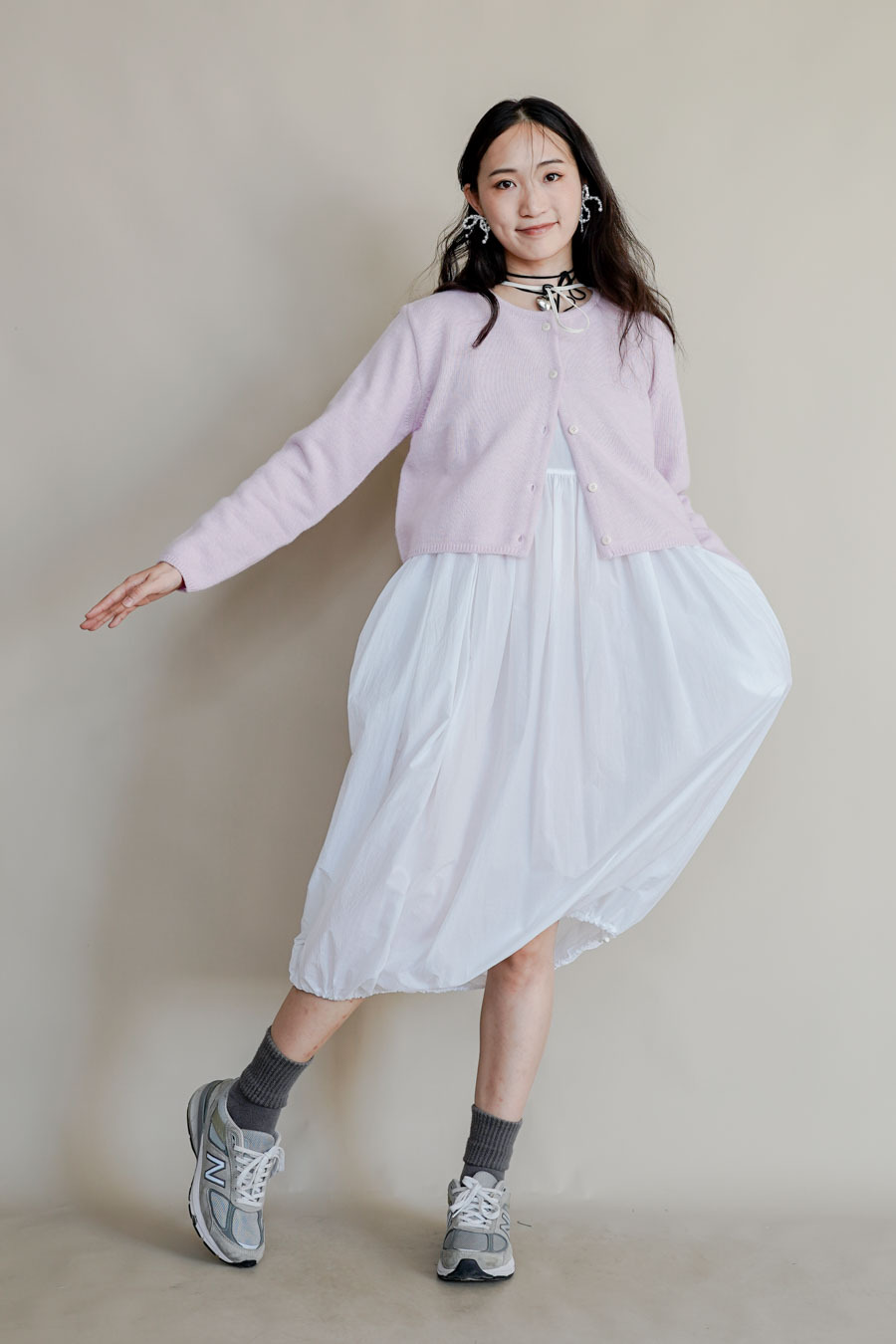 Woman wearing a pale pink cropped cardigan over a billowy white midi dress with grey socks and chunky sneakers