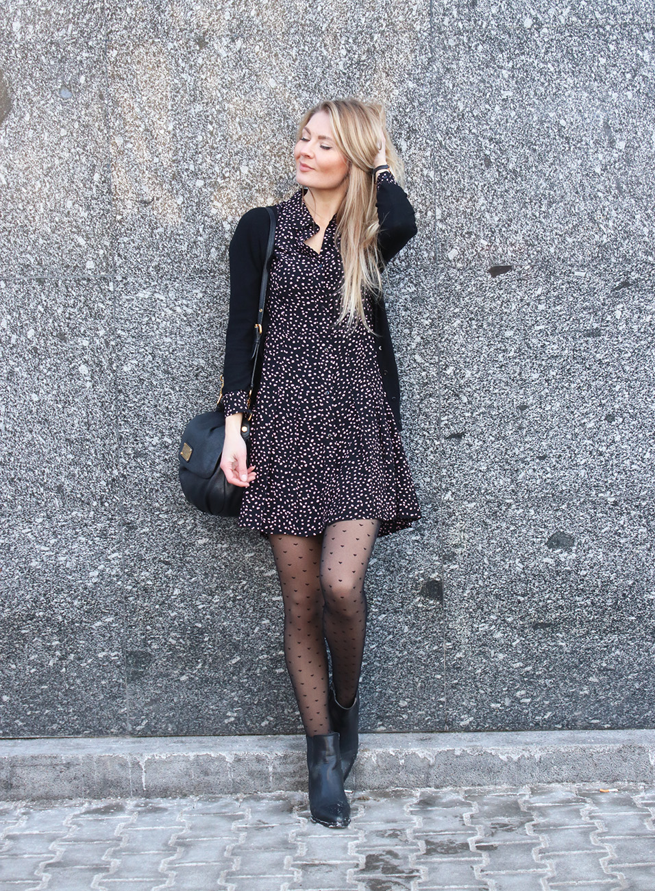 Woman in a black polka-dot mini dress with dotted tights, a black cardigan and ankle boots