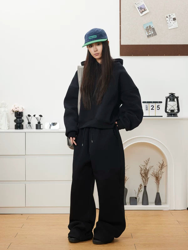 Woman wearing an oversized black hoodie, black wide-leg sweatpants and a baseball cap