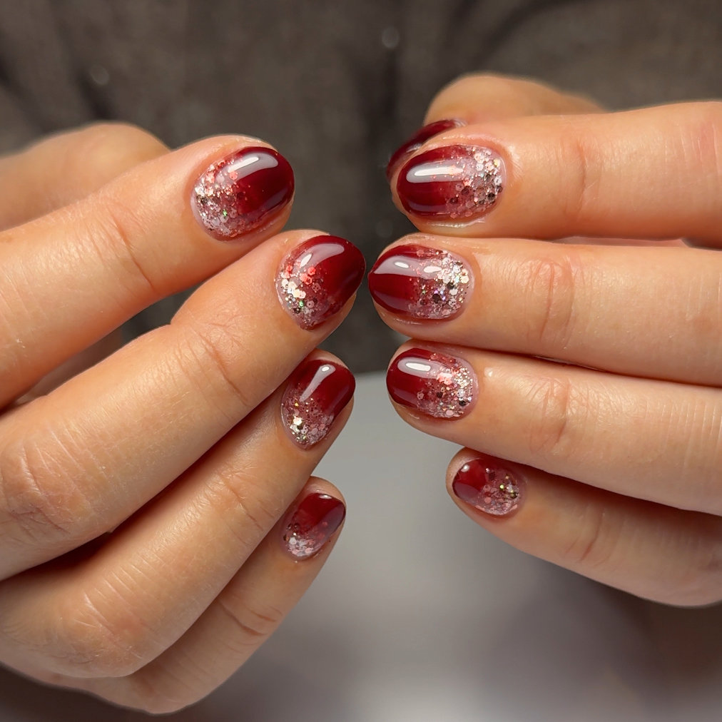 Short oval nails in deep wine red with a chunky silver glitter fade rising from the cuticle