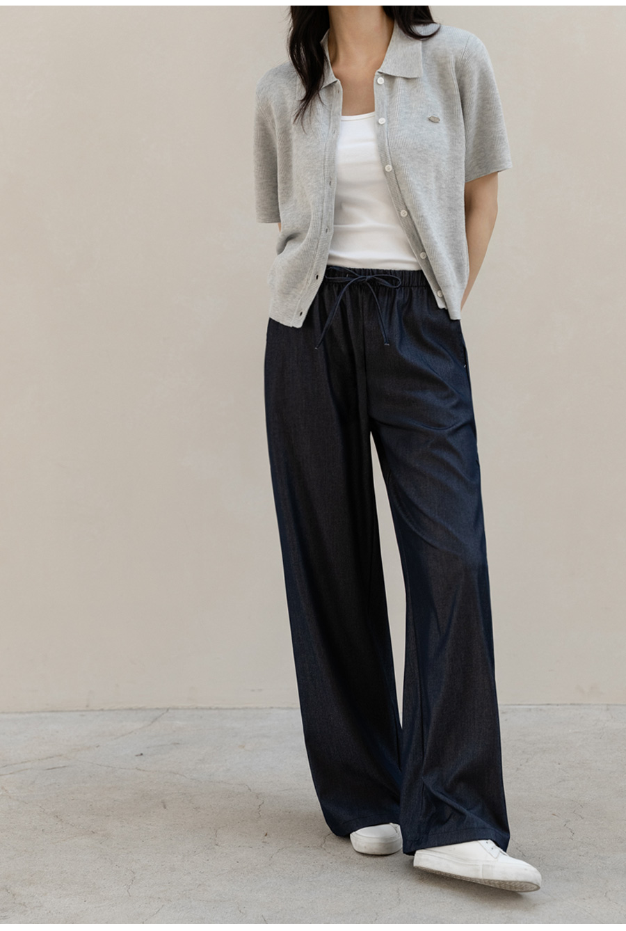 Woman in a grey short-sleeve cardigan over a white camisole with dark wide-leg trousers