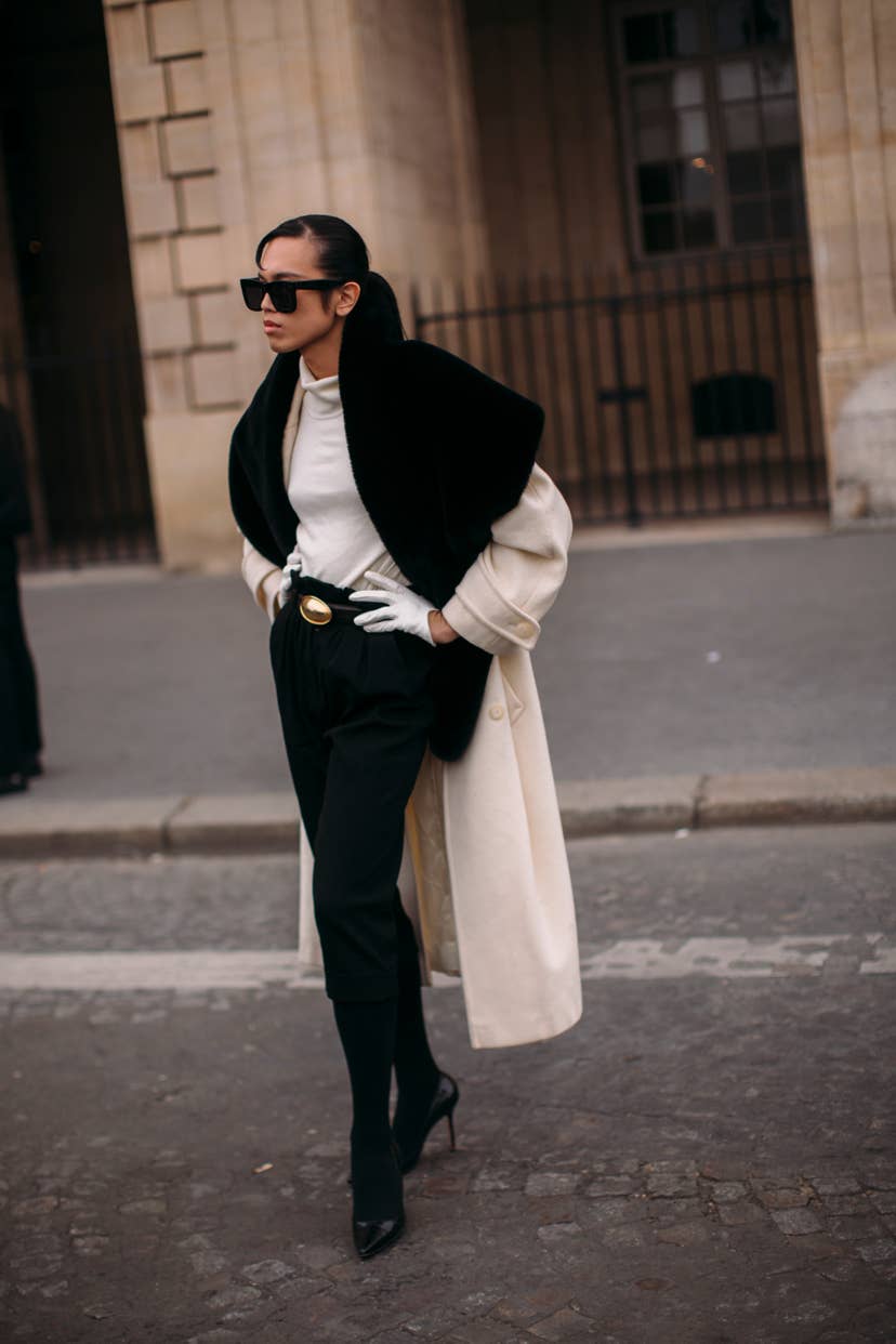 Woman wearing a cream coat with a black faux fur collar and tailored black trousers at Paris Fashion Week