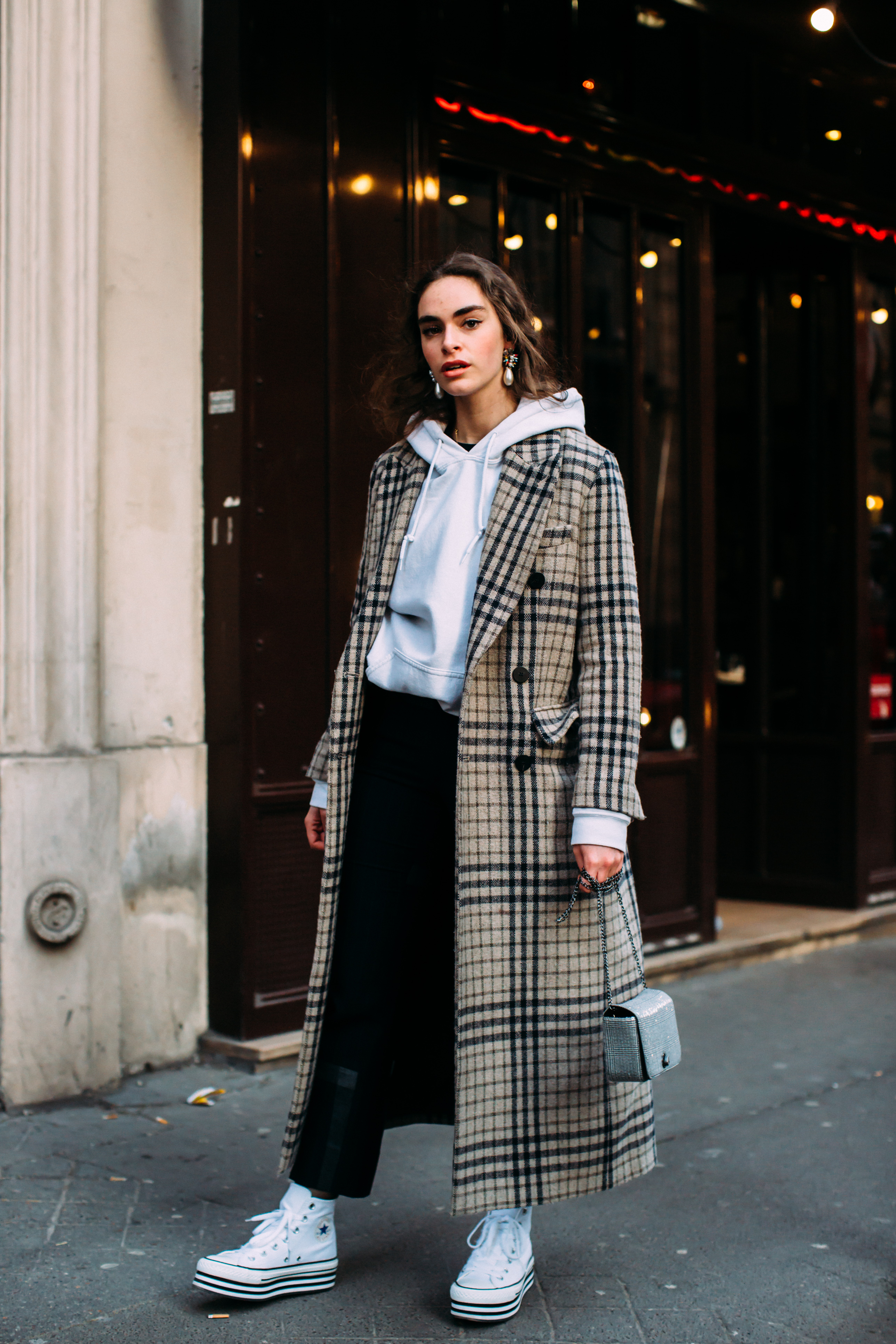 Woman in white hoodie under checked wool coat with platform sneakers in Paris