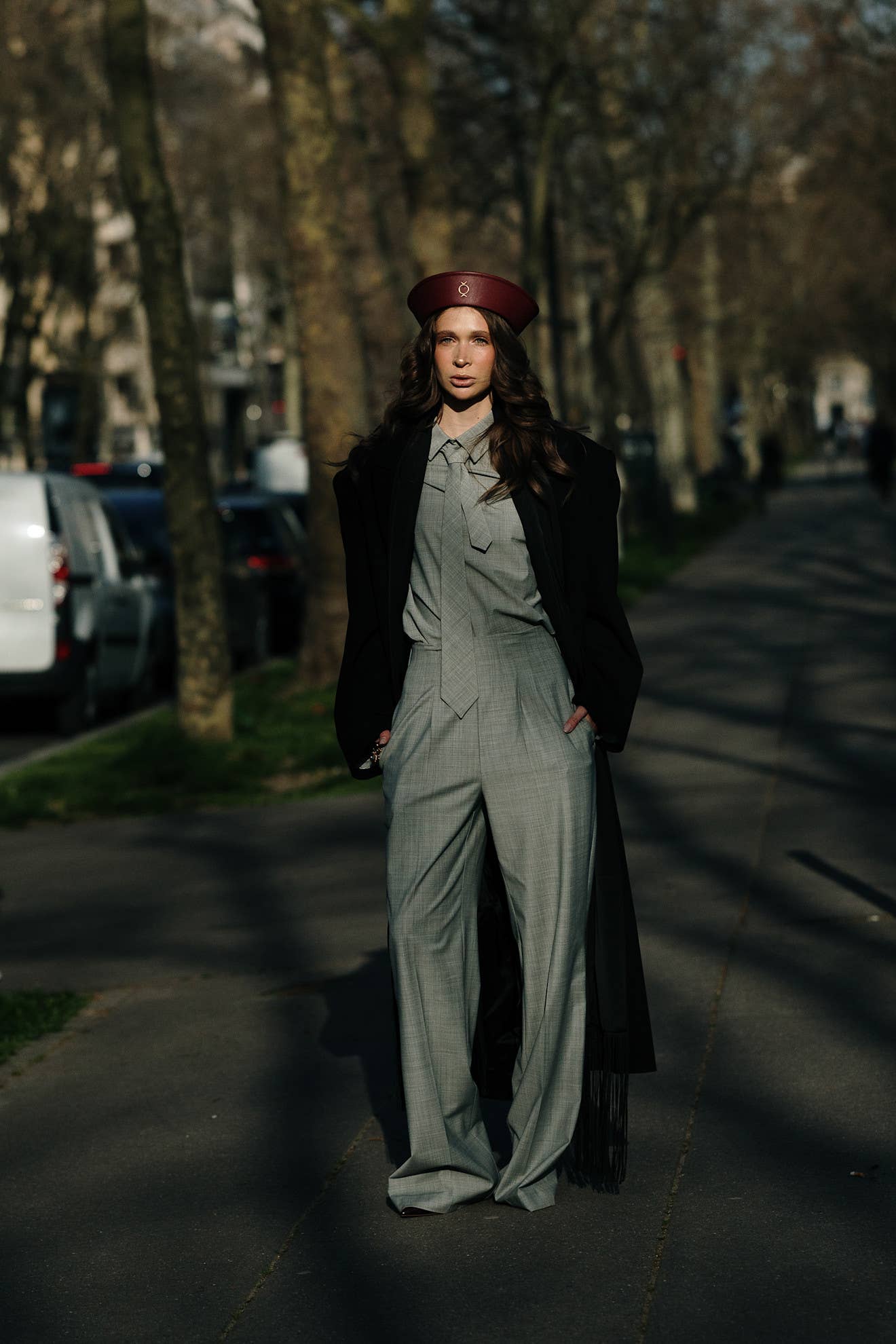 Woman wearing a burgundy leather beret with a grey plaid suit and black coat at Paris Fashion Week