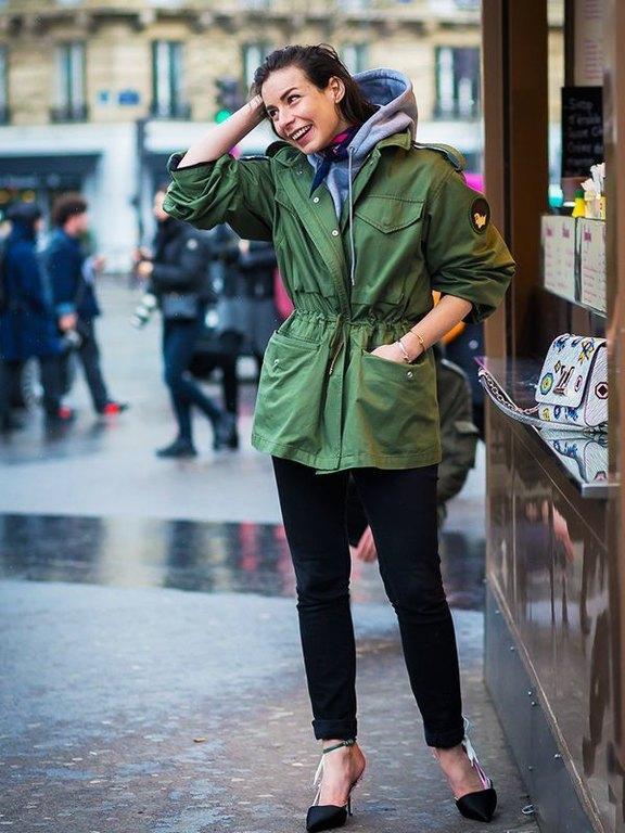 Woman in a cinched-waist green parka over a hoodie with black jeans and heels