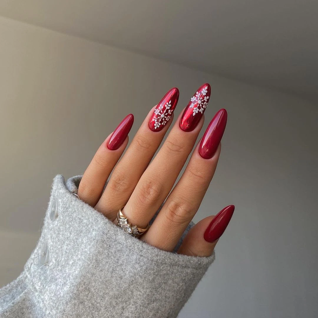 Long almond nails in metallic chrome red with white snowflake accents on two nails