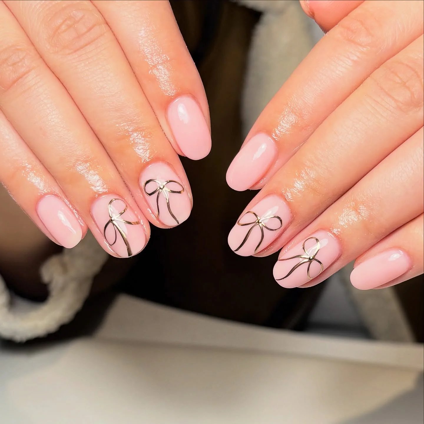 Pale pink oval nails with small gold bow accents near the cuticles