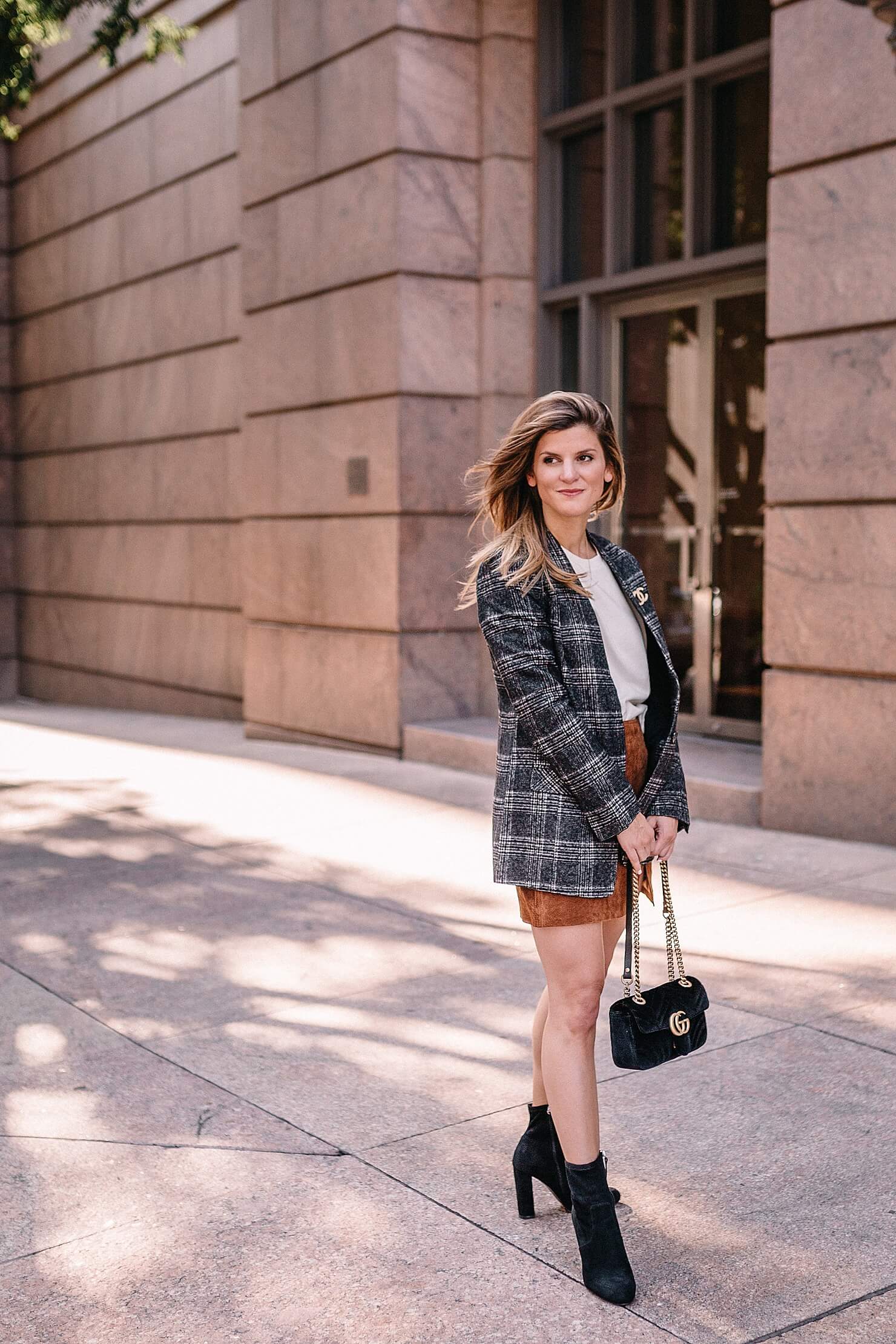 Woman in a black and white plaid blazer with a white top, rust mini skirt, black ankle boots and a black quilted handbag