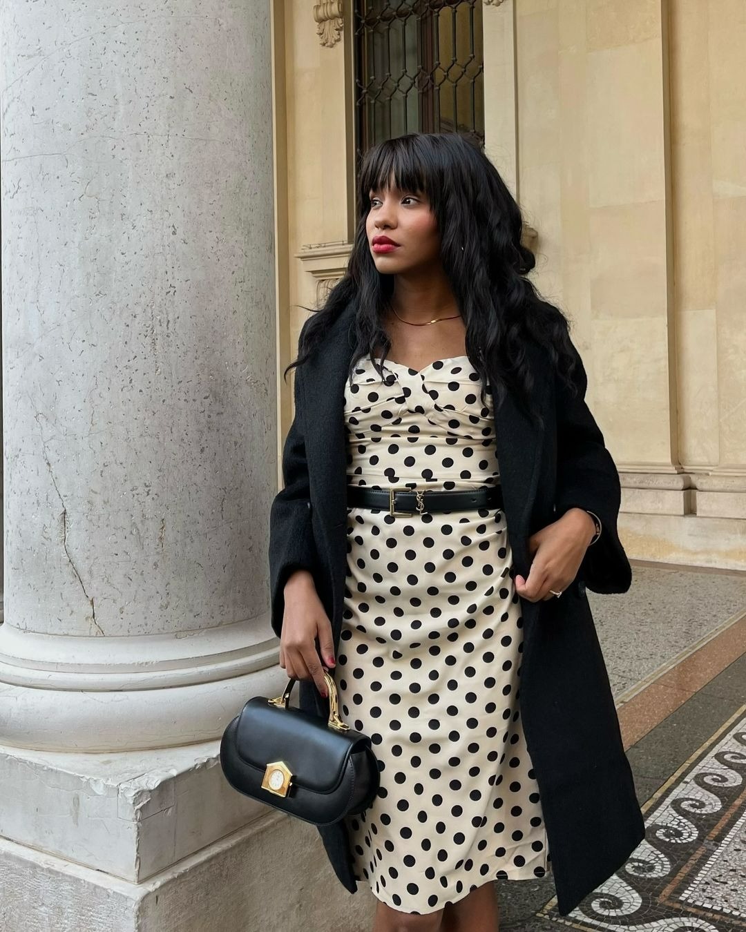 Woman wearing a black wrap coat over a polka dot dress with a black handbag