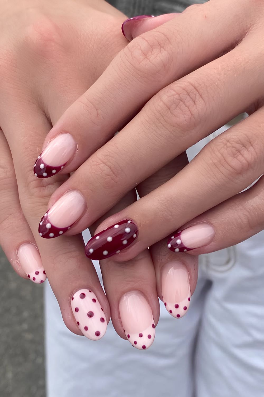 Sheer nude almond nails with burgundy polka dot French tips