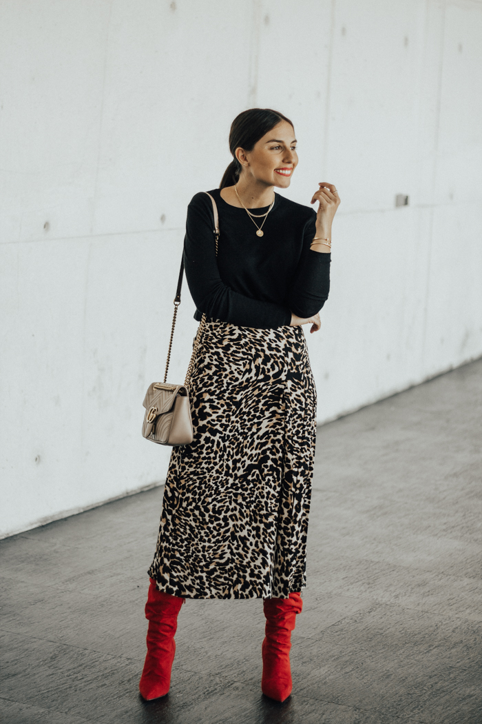 Woman in red slouchy boots with a leopard-print midi skirt, black knit top and taupe bag
