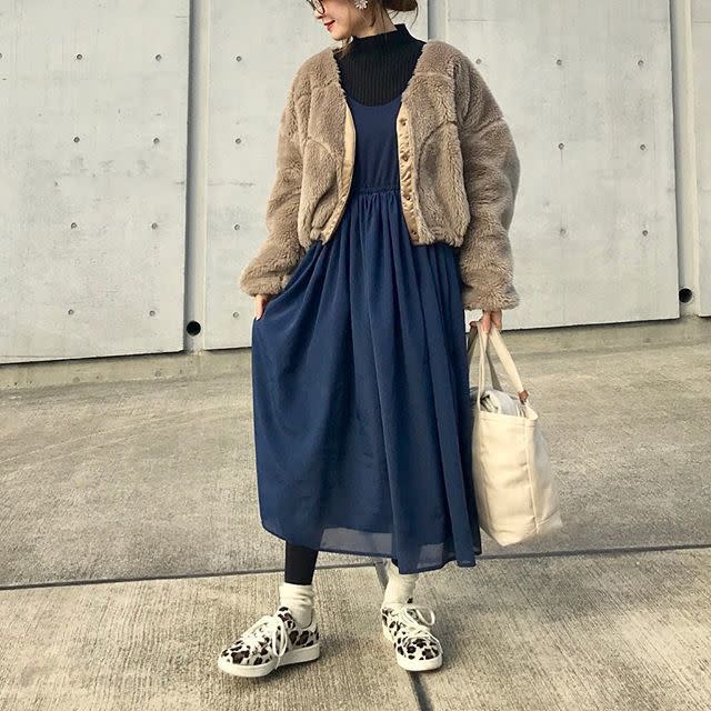 Woman in a taupe fuzzy cropped cardigan over a navy midi dress with leopard-print sneakers and a canvas tote