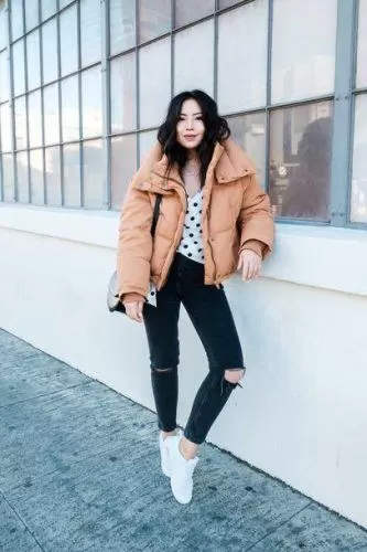 Woman wearing an oversized camel puffer jacket with distressed black jeans