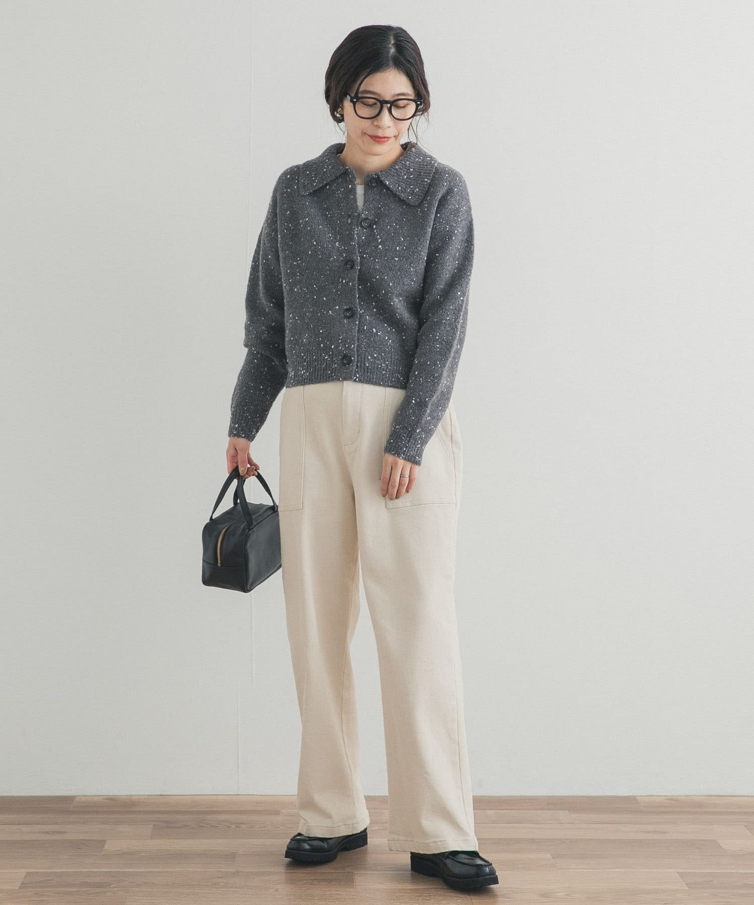 Woman in a grey speckled collared cardigan with cream wide-leg jeans, black loafers and a black mini bag