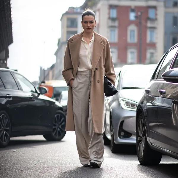Woman in a camel wool coat, cream blouse and wide-leg taupe trousers with dark loafers
