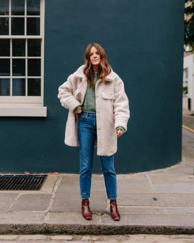 Woman wearing an ivory teddy coat with a sage-green knit top, straight-leg jeans and burgundy ankle boots