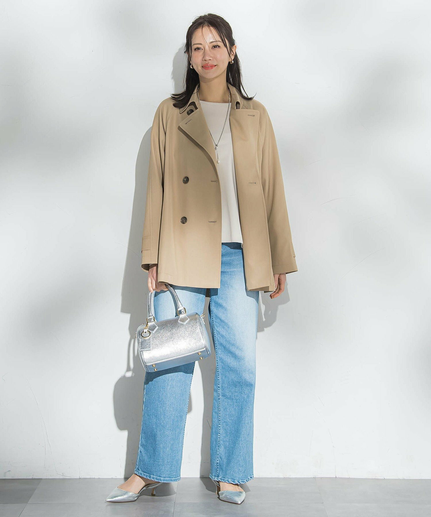 Woman in a cropped beige trench over a white top with light-wash wide-leg jeans, silver heels and a silver bag