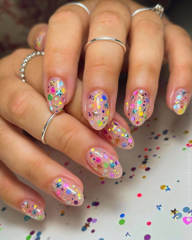 Sheer nails covered in rainbow confetti pieces and metallic gold star accents