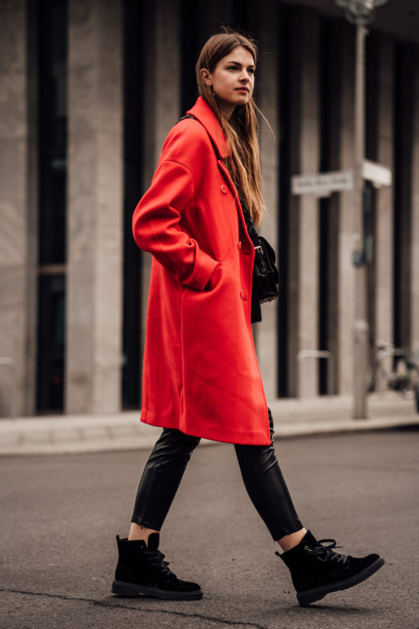 A red coat worn with black leather pants in a street style outfit
