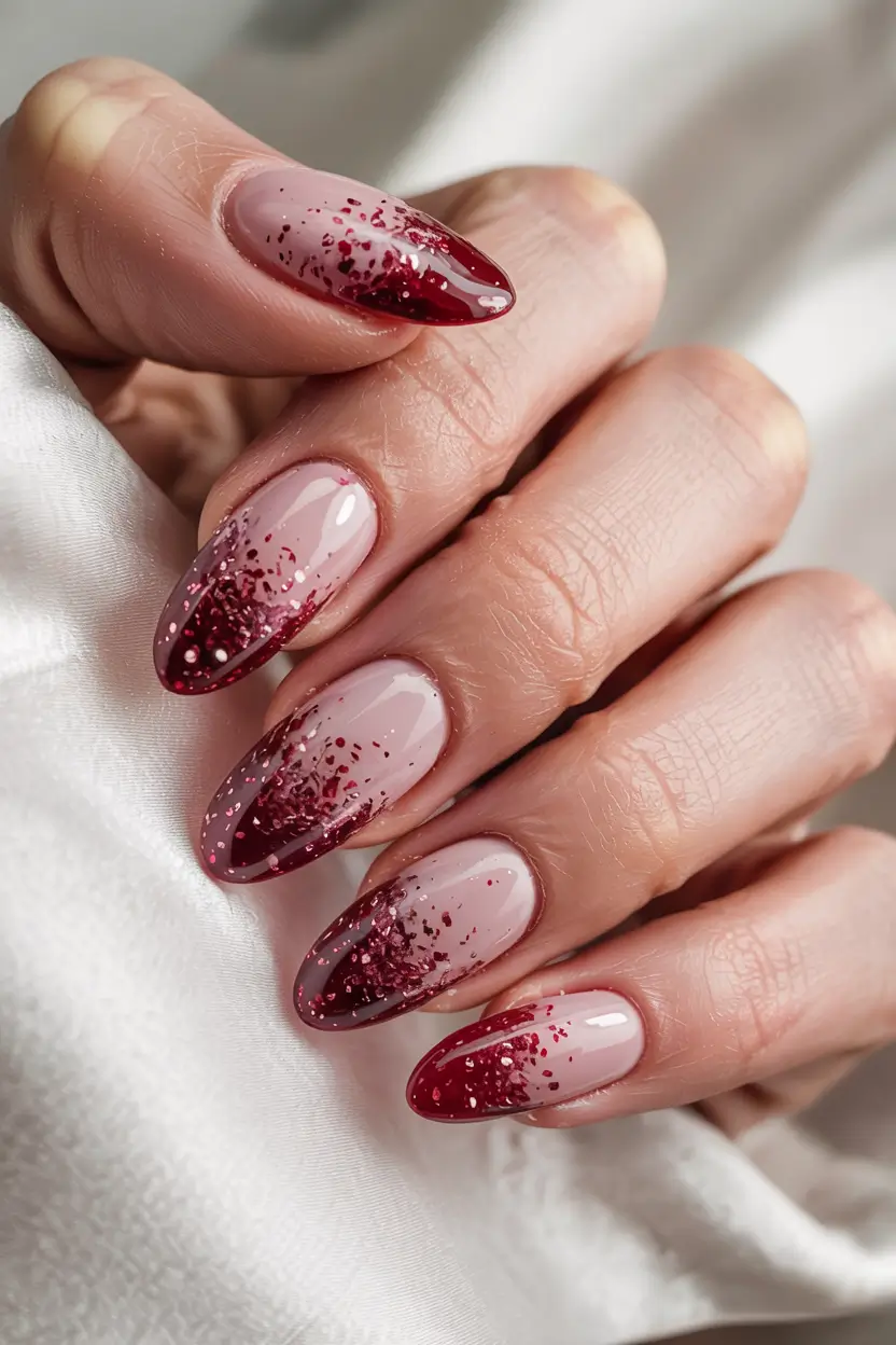 Almond nails with a berry-red to nude ombre fade, scattered glitter concentrated at the darker tips.