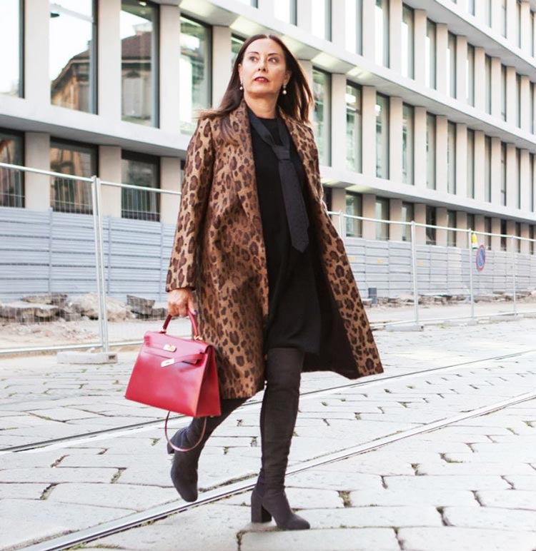 Woman in a leopard print coat with a black outfit and red handbag