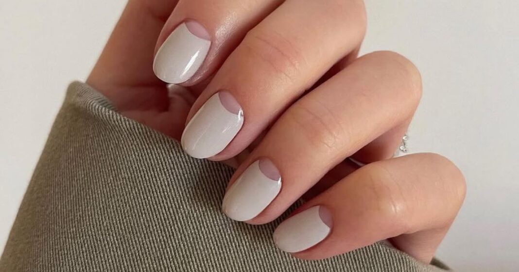 Short soft-white nails with negative-space half moon detail at the cuticle