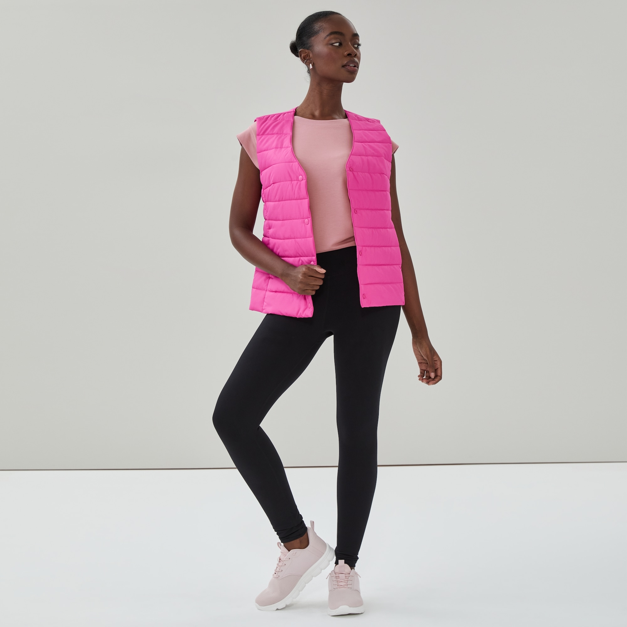Woman wearing a fuchsia lightweight puffer vest over black leggings
