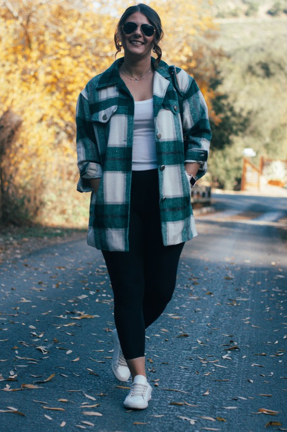 Woman wearing a green and white plaid shacket over a white tank top with black leggings, white sneakers and sunglasses