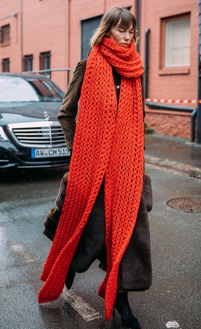 Woman in a dark winter coat with an oversized bright red chunky knit statement scarf