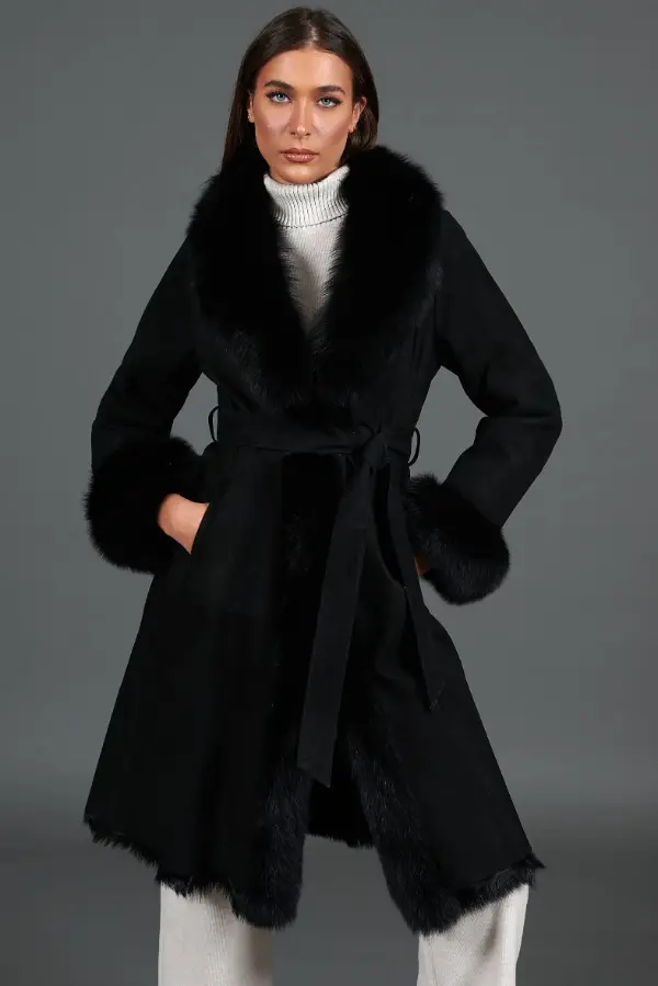 Woman wearing a belted black shearling wrap coat over a white knit