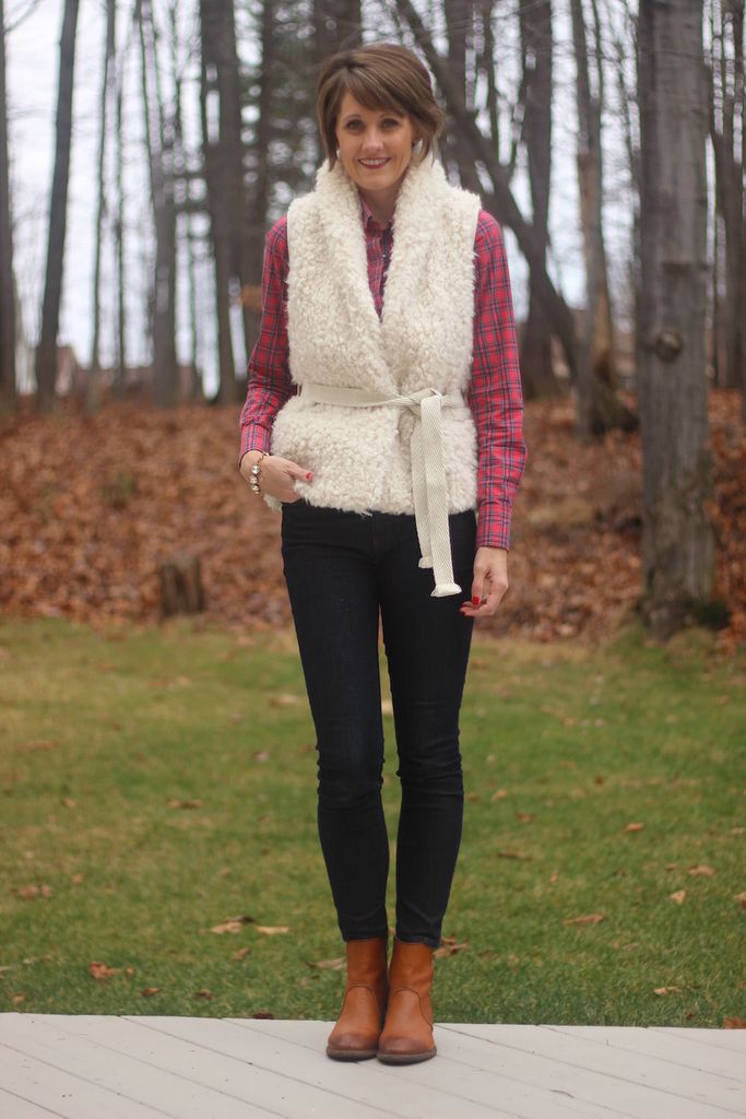 Woman in a cream sherpa vest over a red plaid flannel shirt with black jeans and brown boots
