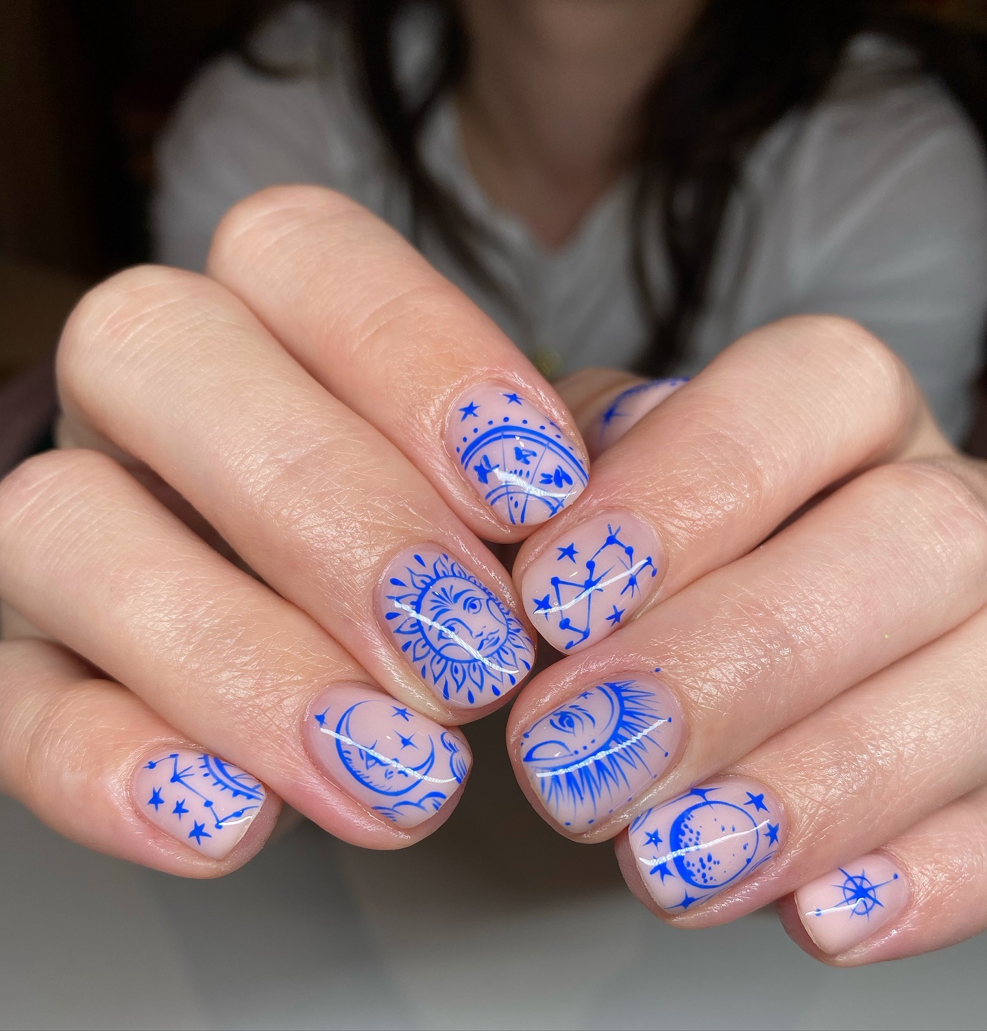 Nude short nails with intricate blue sun, moon, and constellation line art.