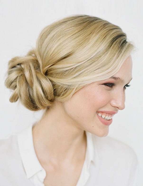 Side-swept low twisted bun in honey blonde hair with soft face-framing waves.