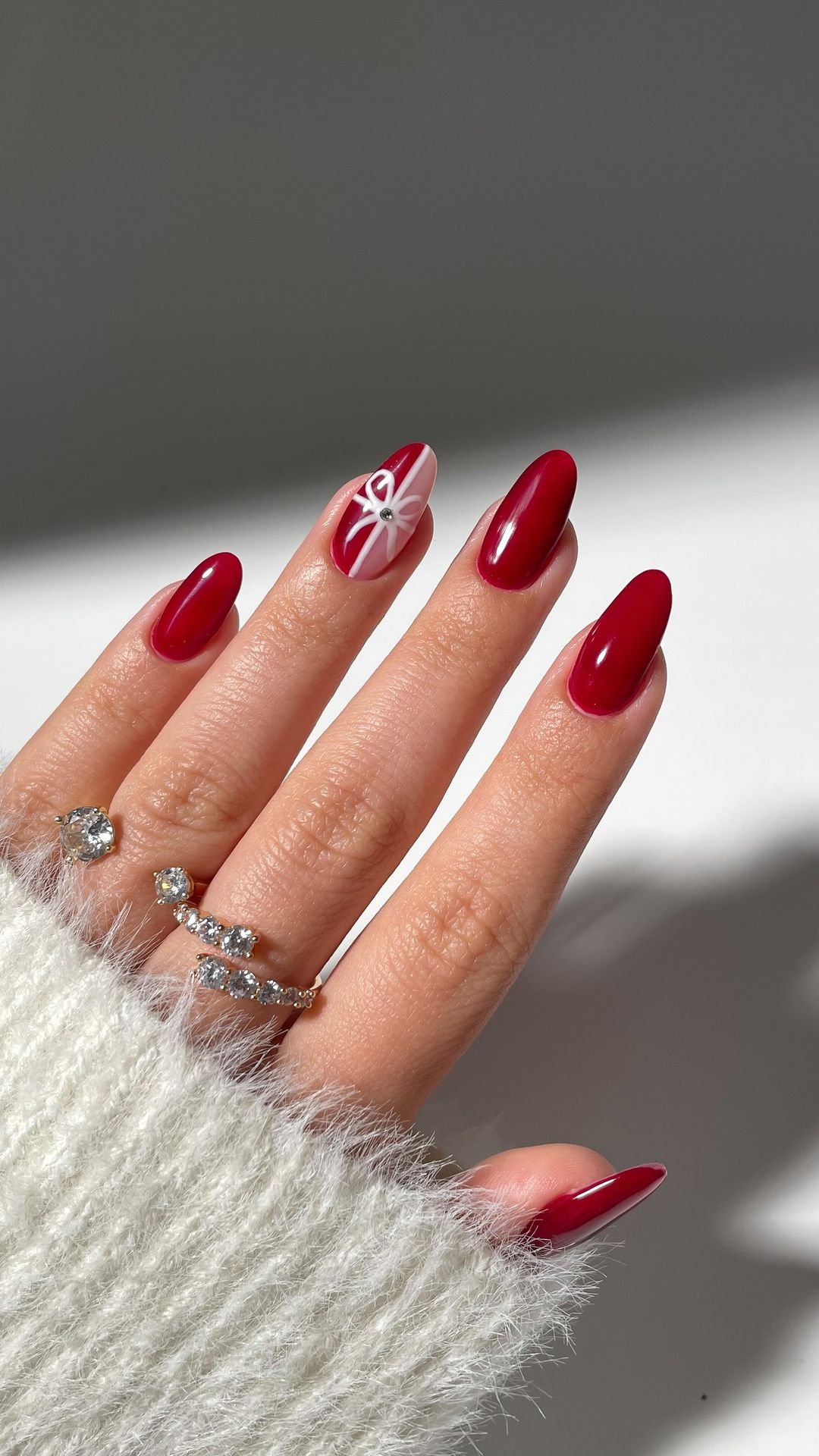 Glossy red oval nails with a white gift-bow accent nail and tiny crystal