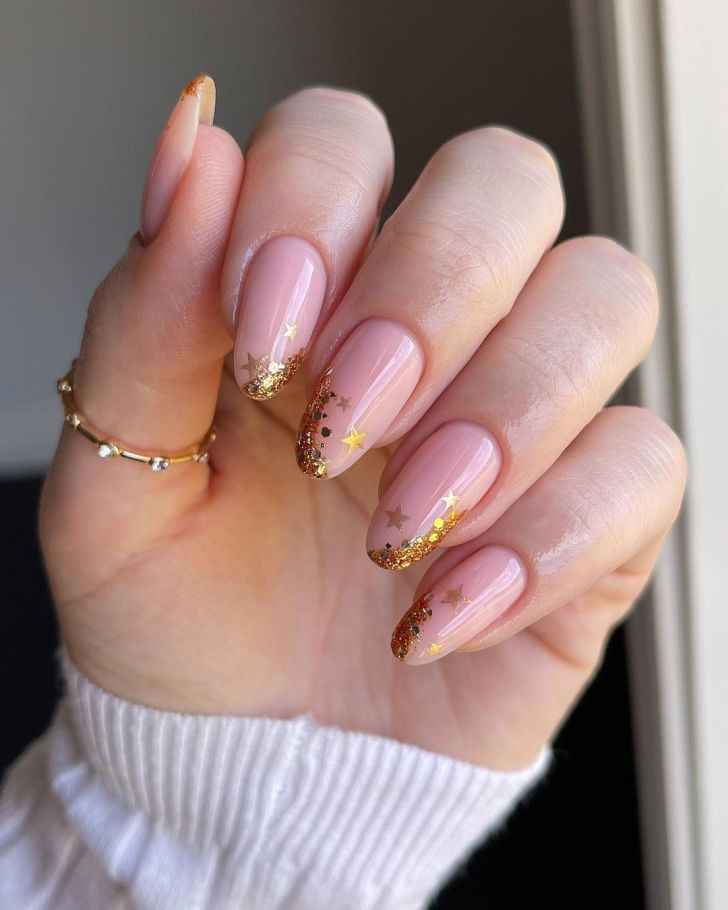 Soft nude almond nails with gold glitter faded tips and tiny gold star decals