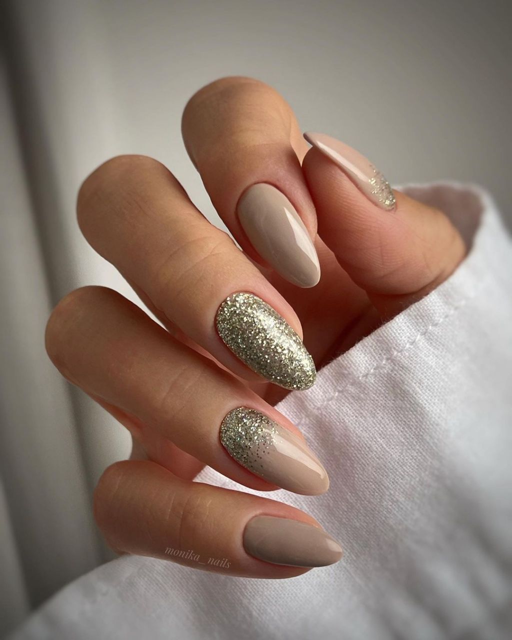 Almond nails in taupe nude with gold glitter fading from the tips on accent nails
