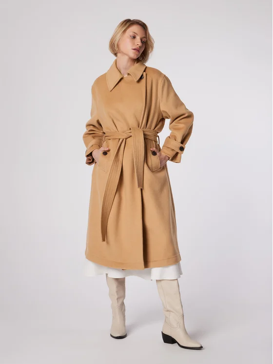 A camel belted wrap coat with patch pockets, worn over a white skirt with cream knee-high boots.