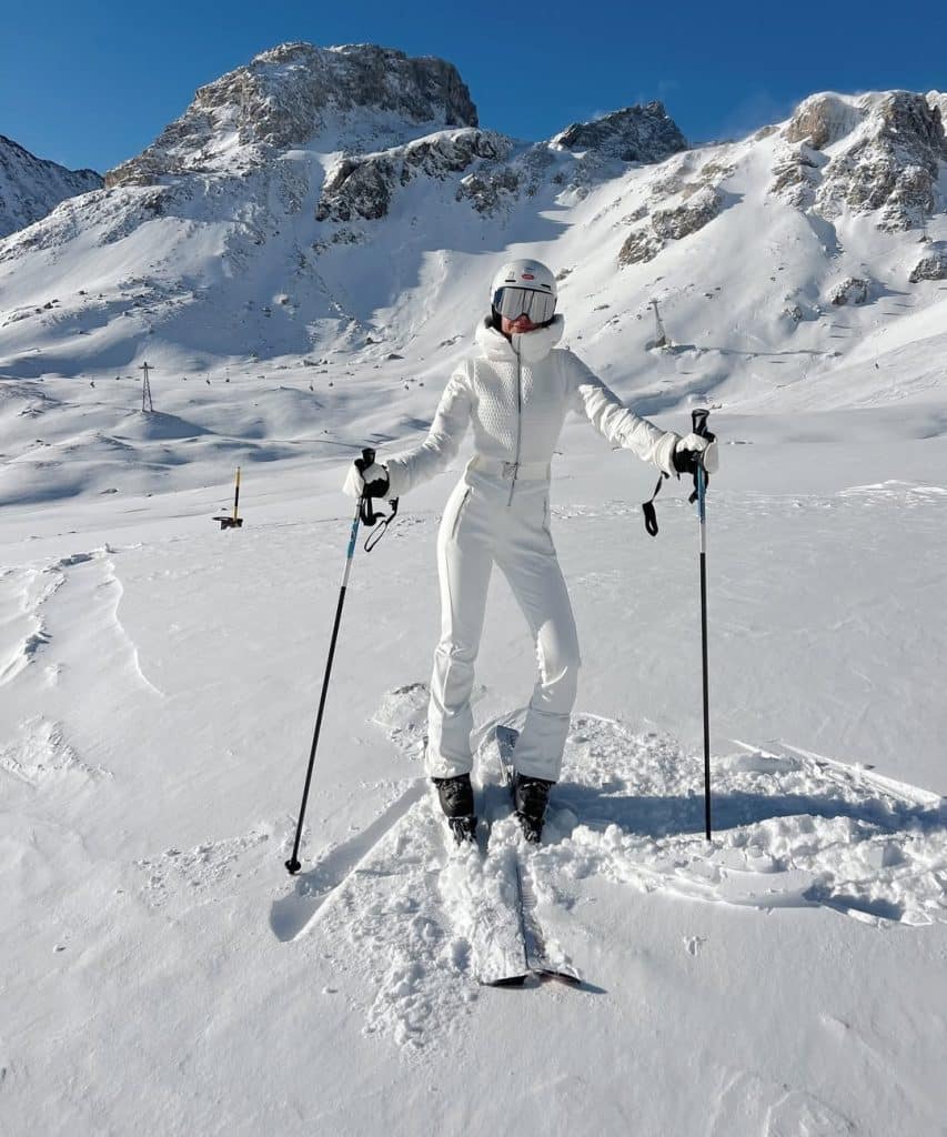 Skier in an all-white quilted ski suit with a white helmet and goggles on a snowy peak