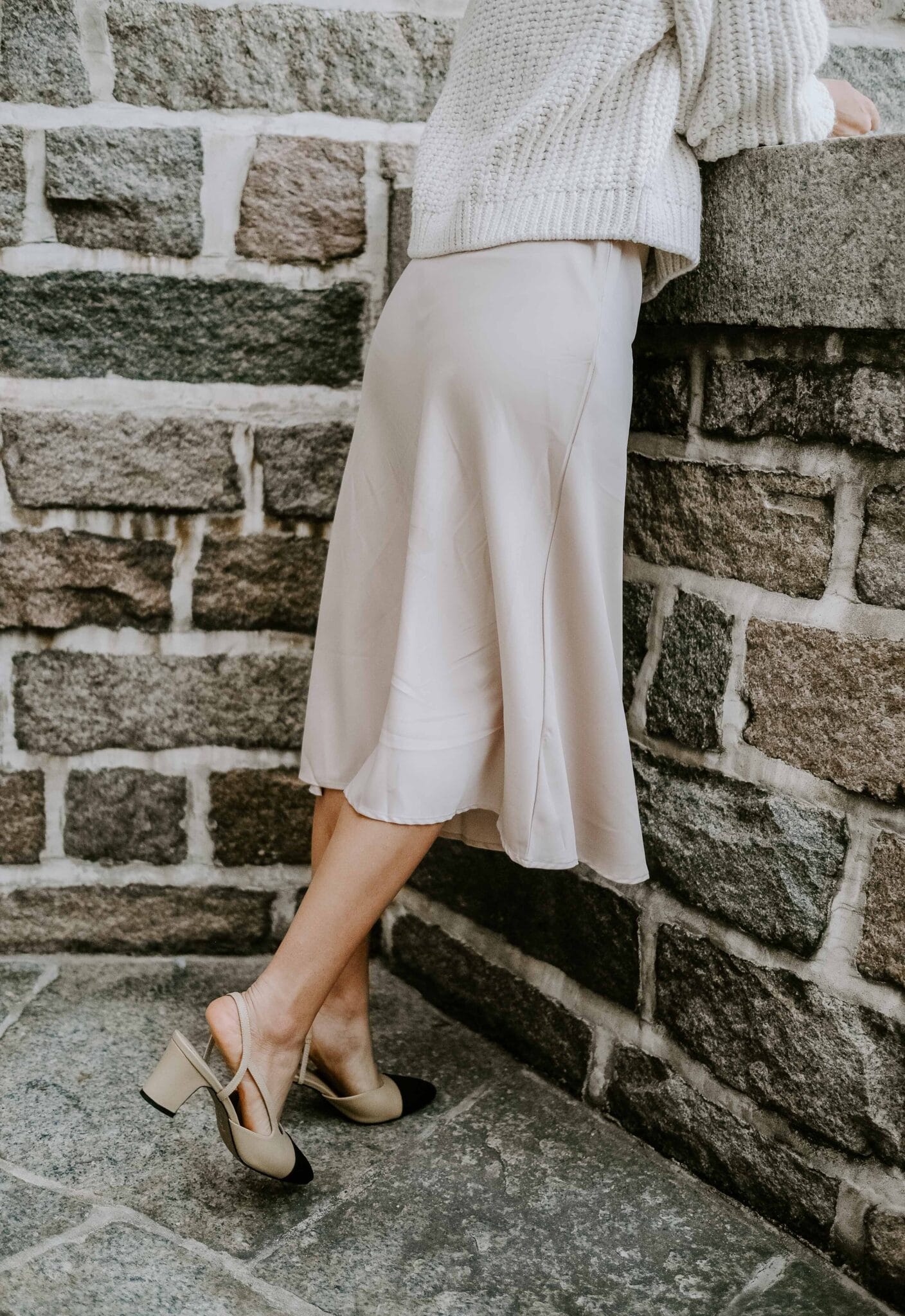 Woman wearing a cream chunky knit cardigan with a champagne satin slip midi skirt and two-tone slingback heels