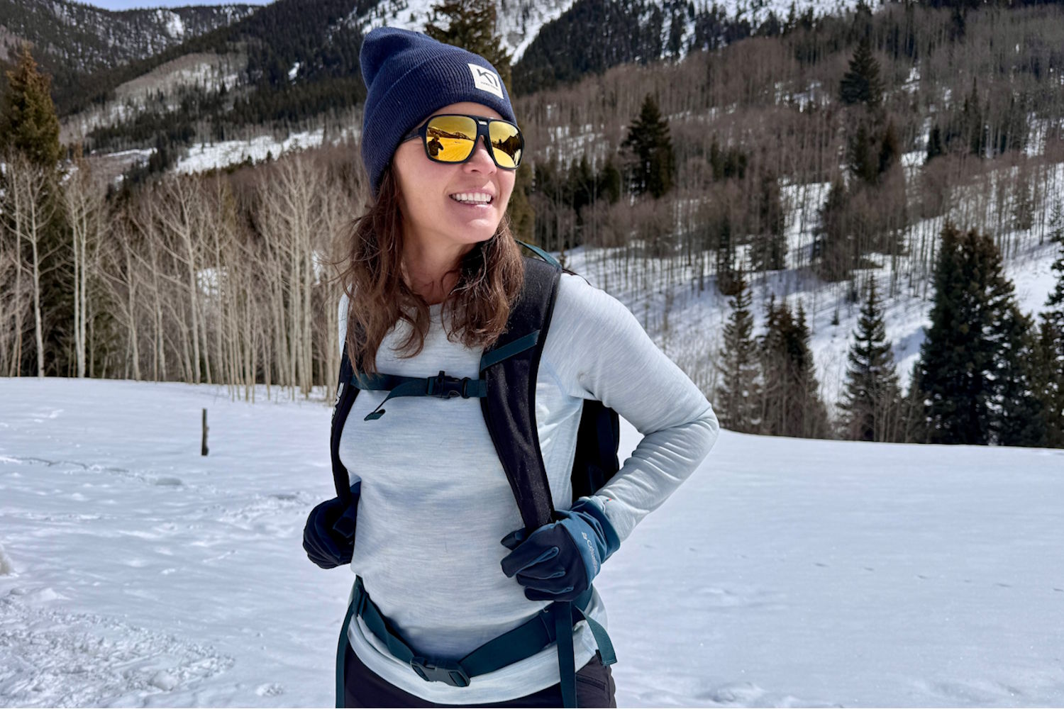 Woman in a merino base layer, beanie and sunglasses on a snowy hike