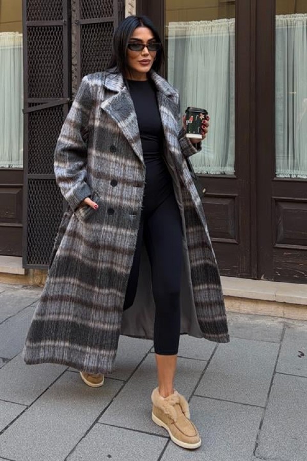 Woman wearing a long grey plaid blanket wool coat with black leggings and tan sneakers holding a coffee