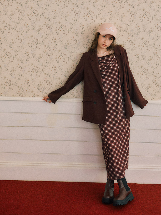 Woman in a brown blazer over a checked midi dress with brown Chelsea boots and a cap