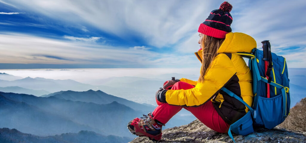 Woman in a yellow puffer and red pants resting at a mountain summit