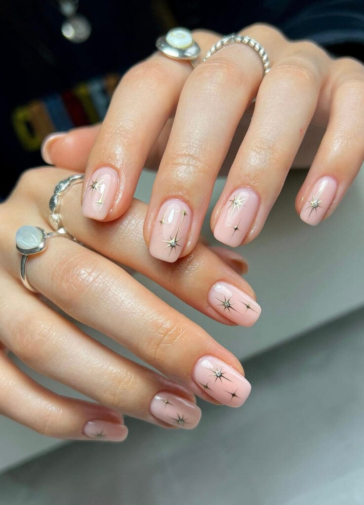 Short round nails in sheer pink with metallic starburst decals.