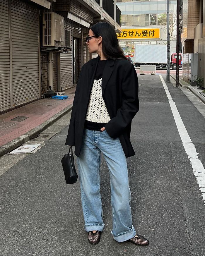 Woman in an oversized black blazer, white crochet knit top, and light-wash wide-leg jeans