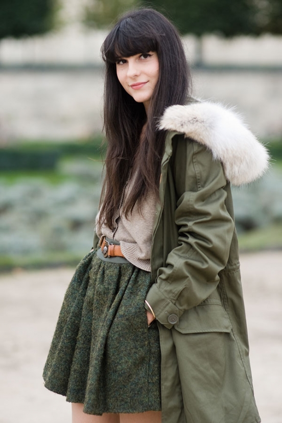 Woman in an olive fur-hood parka with a green wool mini skirt and belt