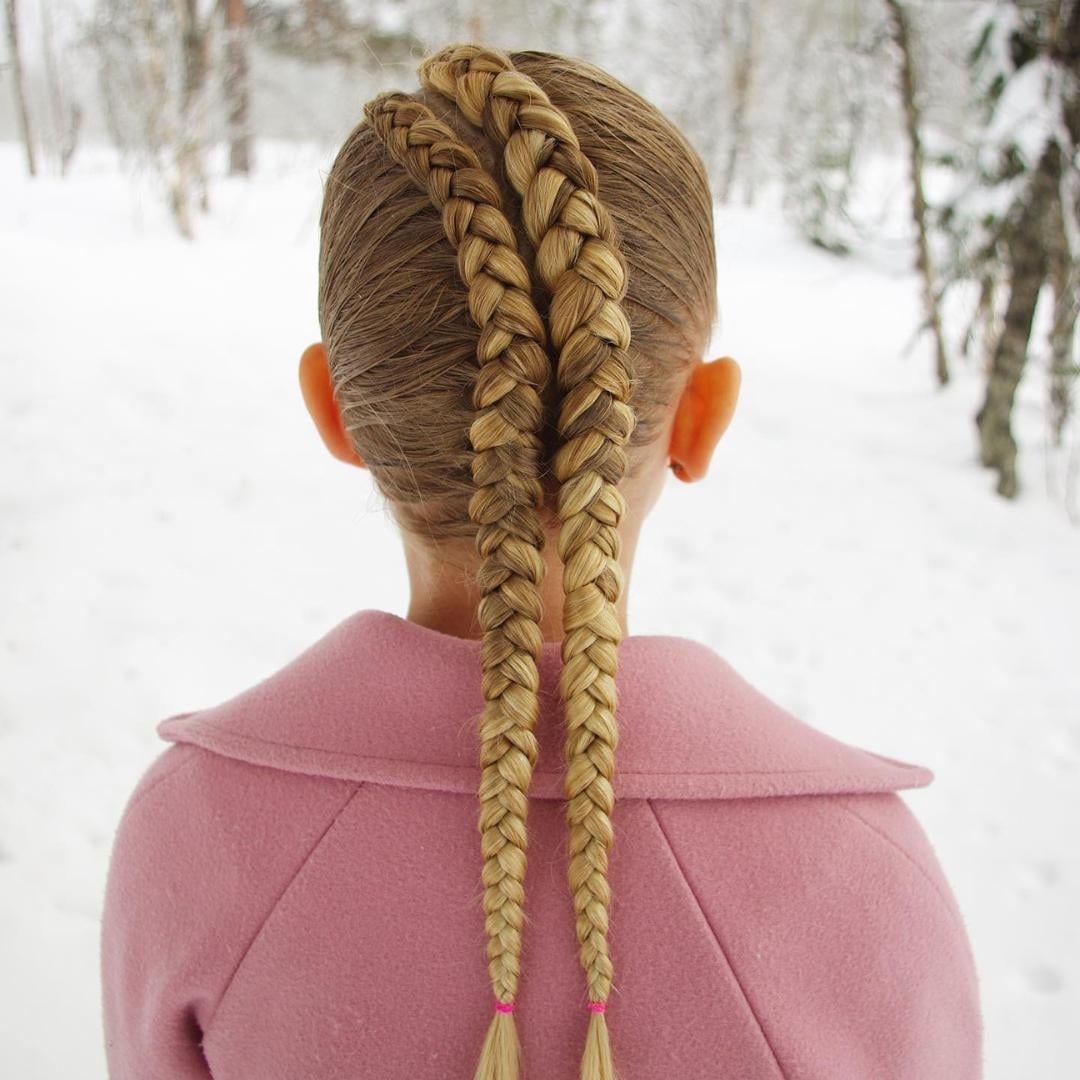 Girl in a pink winter coat with double braided pigtails in a snowy landscape