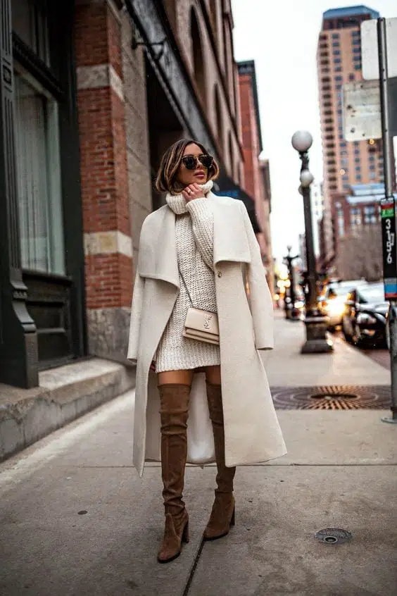 Woman in brown suede over-the-knee boots with a white turtleneck sweater dress and long white coat