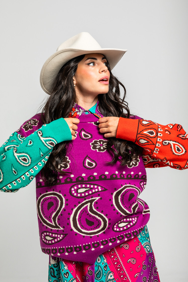 Woman in a multicolor bandana-print sweater and cream cowboy hat in a studio portrait