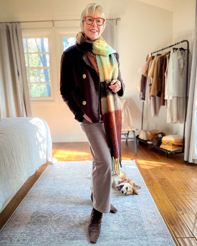 Woman in a dark brown cropped jacket with a colorful striped scarf and taupe trousers